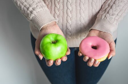 Woman holding a doughnut and green apple. Concept of healthy and unhealthy foodの写真素材