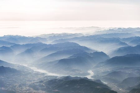 Landscape aerial view of blue Alps mountains with clouds, rivers, and fog.の写真素材
