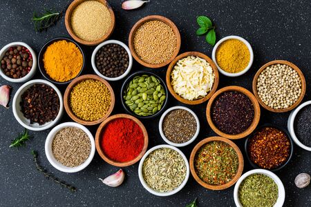 Variety of colorful spices, herbs, and seeds on black stone background.の写真素材