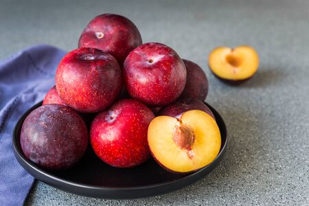 Red organic plums against grey stone background.の写真素材