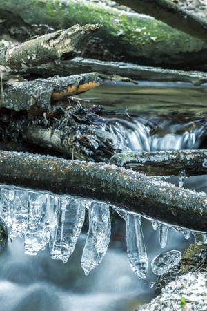 Icicles on Branch Over Frozen River. Long Time Exposure. Winter Landscape Detail.の写真素材