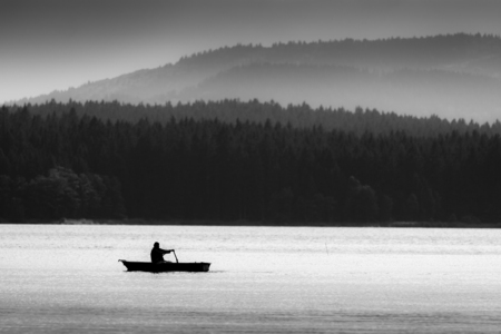 Man on Boat Silhouette. Nature Landscape with Water Surface and Mountains, Forests on Background.の写真素材
