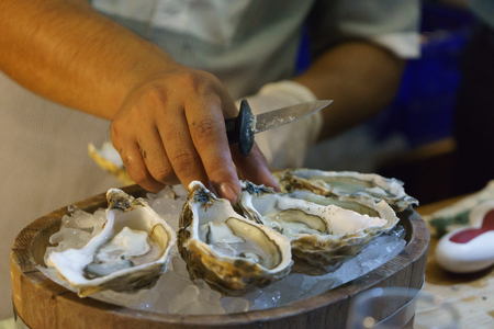 a man putting down oyster after shuck, put oyster on ice in a wood basket, knife is still in his...