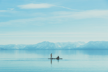 a women in bikini and a man are in small boat in a big lake with snow mountain back ground and clear skyの写真素材
