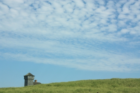 Old lighthouse by the sea with deep blue sky and green grass の写真素材