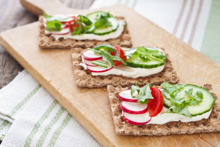 Crispbread with cream and fresh tomatoes, radish, cucumber and arugulaの写真素材