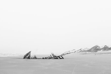 Monochromatic, black and white scenic view of wide empty beach, Atlantic Ocean and wooden ship wreck, abandoned boat skeleton. Solitude nostalgic seascape background. moroccoの写真素材