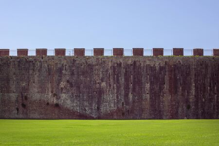 Medieval defensive wall background with green grass and blue sky. Historical city wall backdrop. Old...