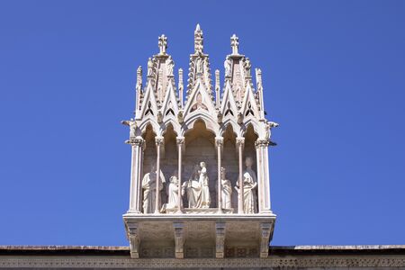 The sculpture of Holy Family over the entrance of the ancient Monumental Cemetery. Architectural detail above entrance to Camposanto Monumentale. Piazza dei Miracoli, Pisa, Tuscany, Italy. Blue sky.の写真素材