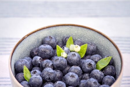 Close-up of bowl with blueberry fruits with green leaf and flower on the kitchen table with tablecloth.の写真素材