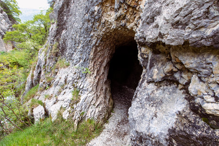 Rock wall with a dark hole, entrance to the cave in Jura mountains, hiking trail, Gorges de Court, Switzerlandの写真素材