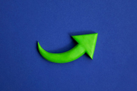 Vibrant green arrow pointing up. 3D mockup, plasticine arrow sign pointing increasing direction on blue background. Development concept, business success, prosperity and growth.の写真素材