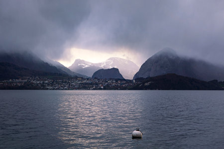 Lake Thun dramatic sunset. View on Alps range with gloomy foggy light effect. Alpine moody cloudscape.の写真素材
