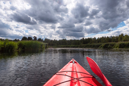 Kayaker point of view. Kayak bow with a view on the river landscape and rushes. River kayaking during summertime concept. Active vacations in wild nature.の写真素材