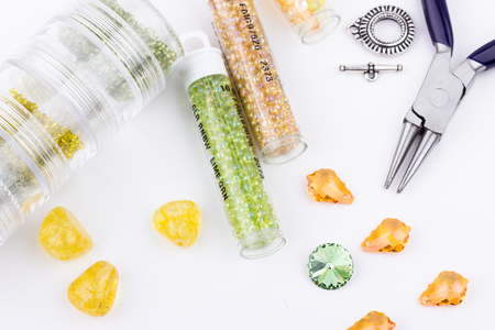 Jewelry making and beading process. Glass seed beads, beads, crystal stones, silver toggle, jewelry bag and pliers on white background. Selective focus.の写真素材