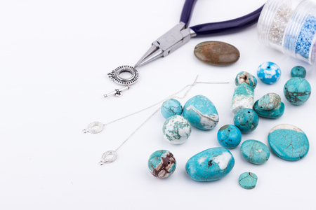 Jewelry making and beading process. Glass seed beads, turquoise stones, silver toggle, earings and pliers on white background. Hobby, handmade,fine arts. Selective focus.の写真素材