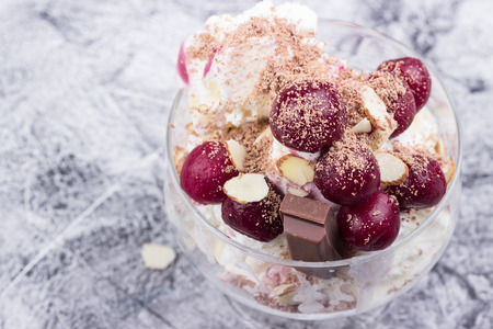 Ice-cream with white and dark chocolate, almond petals, cherries in glass on grey background. Selective focus.の写真素材