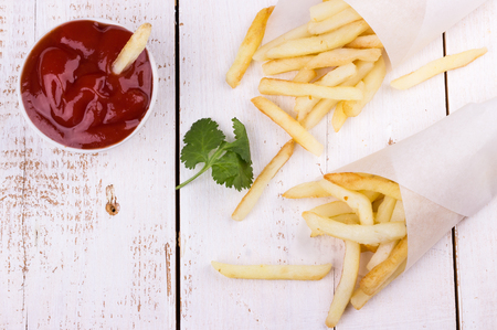 French fries in paper bags with ketchup on white wooden background. Fast food. Selective focus.の写真素材