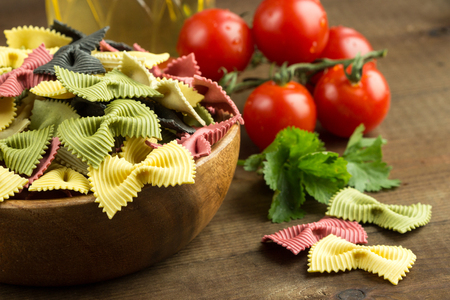 Colored Italian Farfalle Pasta in a Wooden Bowl with Fresh Tomatoes, Olive Oil and Cilantro on a tableの写真素材