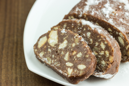 Chocolate italian salami slices with biscuits and hazelnuts  on white plate. Sweet dessert. Selective focus.の写真素材
