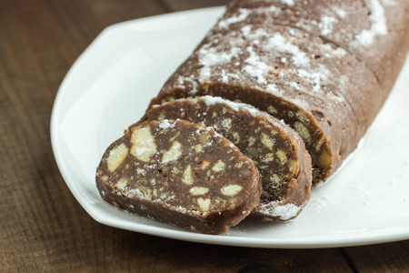 Chocolate italian salami slices with biscuits and hazelnuts  on white plate. Homemade dessert. Selective focus.の写真素材