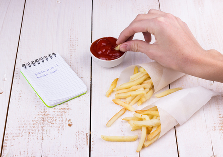 Fast food, unhealthy eating, teenager is dipping french fries potatos into tomato ketchup on white...