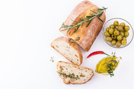 Ciabatta bread, olives in glass bowl, rosemary, red chili pepper and olive oil on white background. Top view.の写真素材