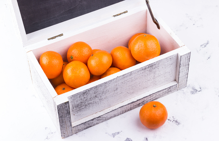 Orange tangerines in white wooden box on white marble background.の写真素材