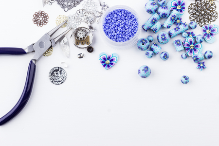 Jewelry making and beading. Seedbeads, metal components, polyclay purple blue flower beads mix, pliers on white background. Selective focus. Top view.の写真素材