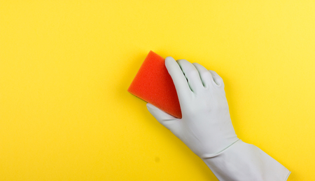 Cleaning, housekeeping, home, clean up concept. Hand in rubber glove cleaning surface with orange sponge. Flat lay. Yellow background.の写真素材