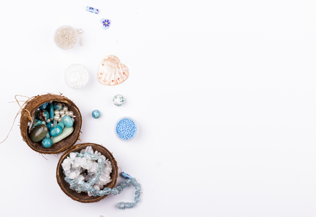 Feminine workplace in blue and aqua colours in flat lay style. Gemstones, glass beads, shell beads in coconut halves for handmade jewelry making on white background. の写真素材
