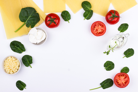 Ingredients for spinach lasagne- dry sheets, tomatoes, spinach, cheese, oil, white background. Flat lay composition.の写真素材