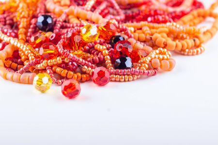 Mix of red and orange stone and glass beads for beading on white background closeup. Selective focus. の写真素材