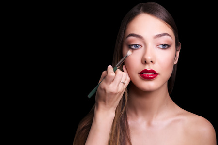 close portrait of beautiful girl making make up. Isolated on black background. Copy space.の写真素材