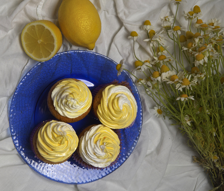delicious freshly baked homemade lemon muffins cupcakes with butter cream with  bouquet of chamomile flowers , copy spaceの写真素材
