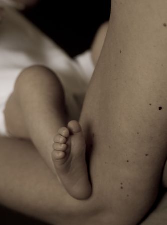 Little 7 days old baby lying securely on mom's arms, against a black background