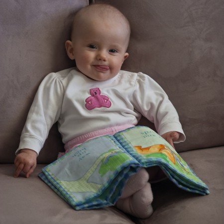 Little baby girl sitting on a sofa and playing with cloth book.の写真素材