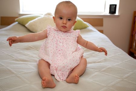 Cute little caucasian baby girl wearing pink dress and sitting on a bed.の写真素材