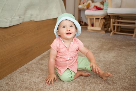 Caucasian baby girl in green hat playing on a floor.の写真素材