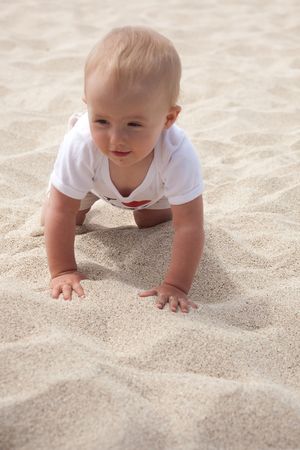 Cute Caucasian baby girl playing with the sand on the beach.の写真素材