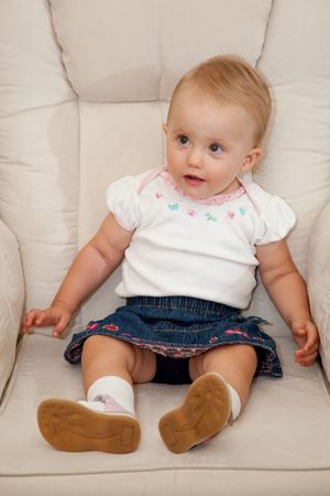 Cute little caucasian baby girl sitting on a chair.