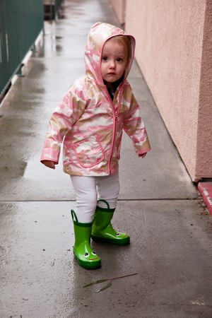 Cute caucasian baby girl wearing pink raincoat and green rubber boots.の写真素材