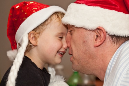 Father playing with duagther wearing read santa hat.