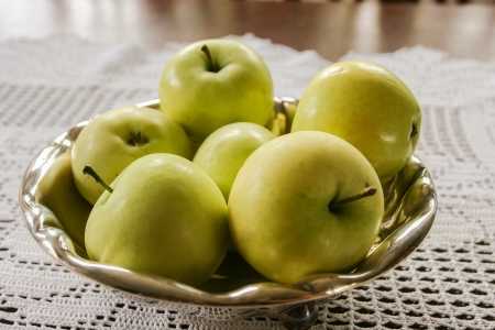 Freshly picked green apples in a metal bowl on a table.の写真素材