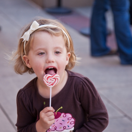 Cute little European toddler girl having fun eating heart shaped lollypopの写真素材