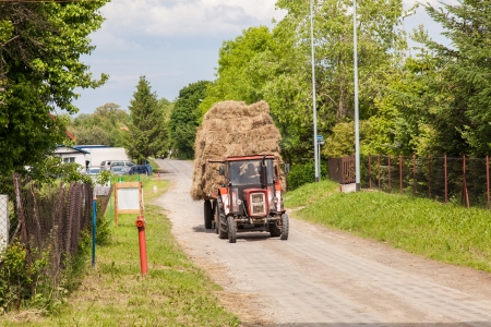 Tractor with large loads of baled hay on a village road.のeditorial素材