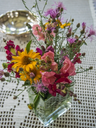 Wild flowers in a vase on a wooden table with white tablecloth.の写真素材