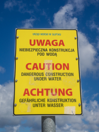 Yellow warning sign about breakwaters in water on Baltic sea coast in Polandの写真素材