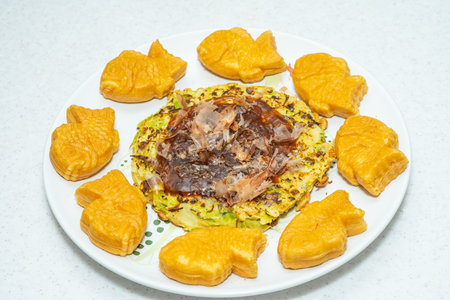 A plate of traditional Japanese food: savory okonomiyaki pancake with bonito flakes, and fish-shaped taiyaki cakes.の写真素材