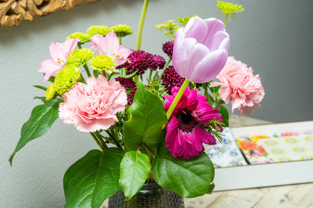 A beautifully arranged bouquet of flowers featuring pink carnations, a purple tulip, and green chrysanthemums. Fresh floral arrangement brings color to the room.の写真素材